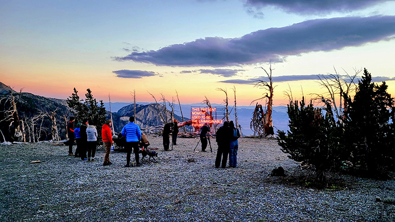 Researchers on top of a mountain setting up a sign that says, "This present moment used to be the unimaginable future."