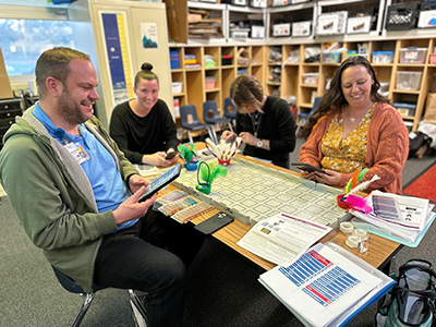 2024 at a glance report Milestone Educators smiling around a table working with tablets and robots during a training.