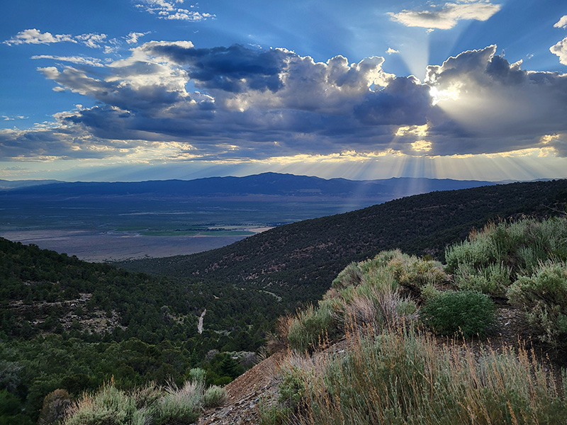 The sun is poking out from behind the clouds in a landscape image of a valley surrounded by mountains.