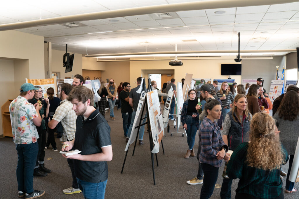 A conference room with researchers mingling and reviewing graduate student poster presentations.