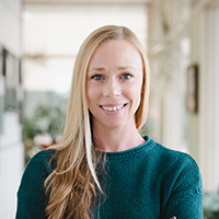 Anne's headshot wearing a green sweater and smiling at the camera with a blurred background.