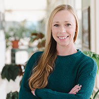 Headshot of Anne Heggli in a hallway with natural light. She is wearing a green shirt and smiling. 