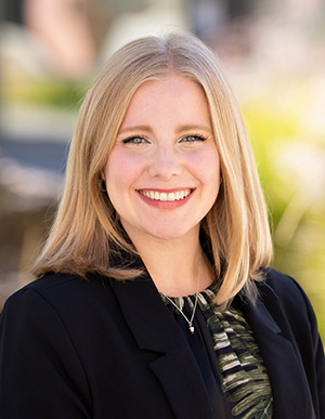 Headshot of Ashley Cornish smiling outside with greenery in the background.