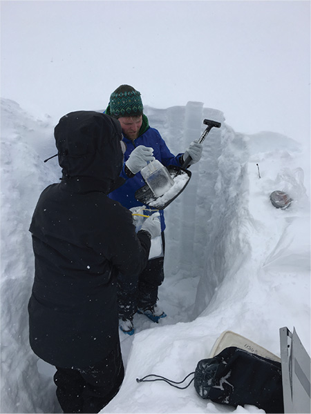 Two researchers collecting samples of snow in a deep snow pit.