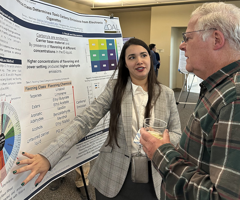 Bianca pointing to a section on her poster presentation and explaining the section to another researcher.
