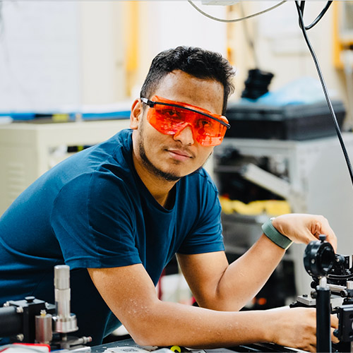 Biographical Prakash Gautam in the lab working with equipment and wearing protective eye covering.