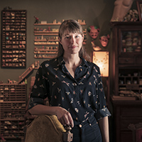 Jessica Oreck posing by a chair in warm light surrounded by her curated collection at the Office of Collection & Design. 