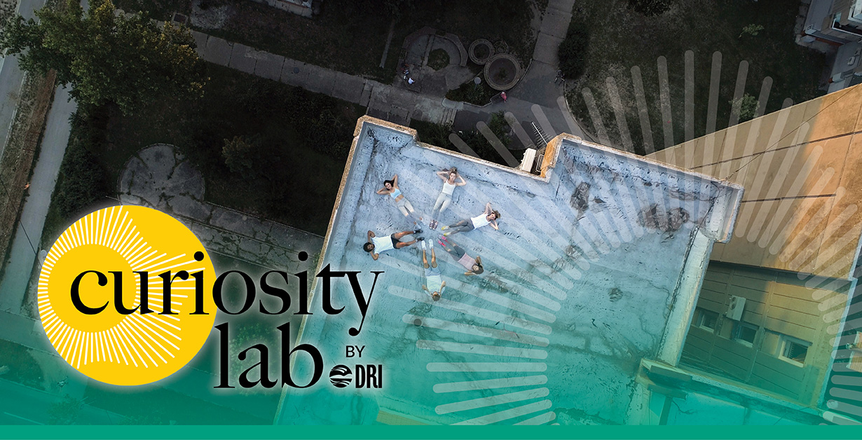 Curiosity Lab logo over an ariel image looking down on a roof top with people laying down in a circle.