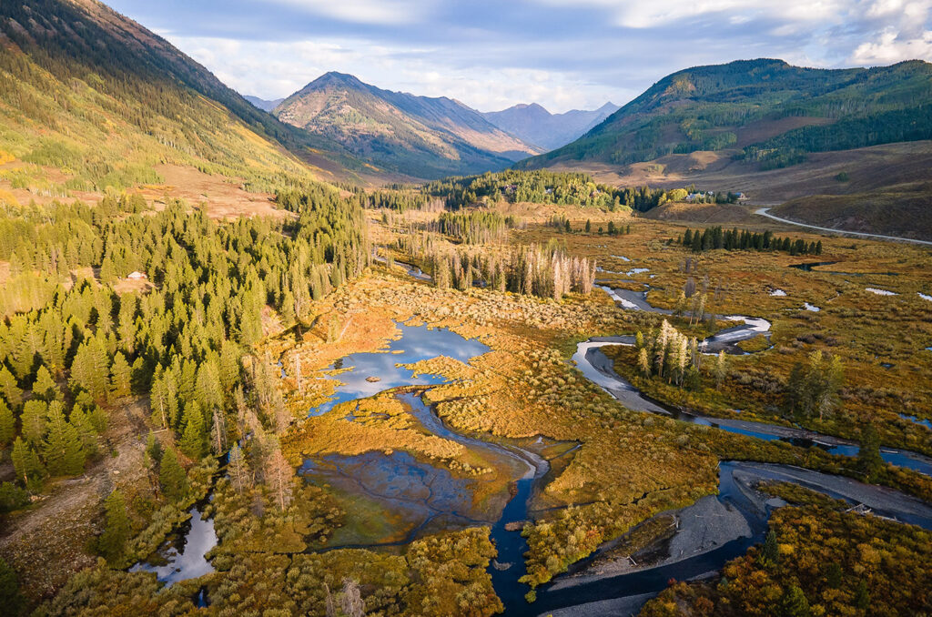 Arial image of a river running through a canyon between mountains with pine trees and scrubs.