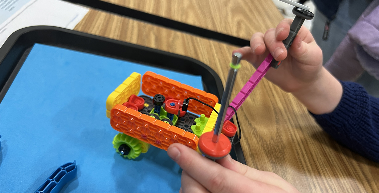 Commuity Engagement DRI STEM Graphic Two hands are working on constructing a small robot on a table.