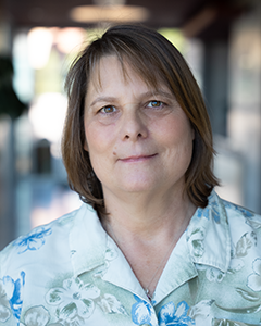 Headshot of Connie outside smiling and wearing a floral button down shirt.  