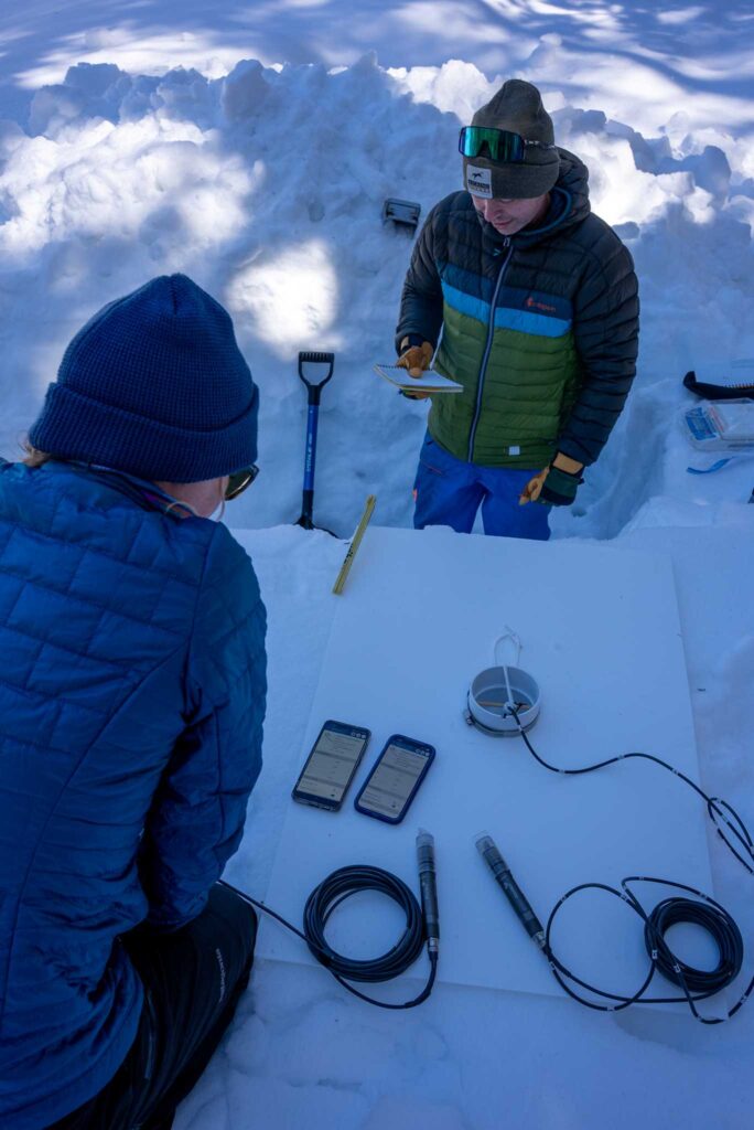Two researchers looking at devices standing in a snow pit.