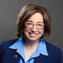 Duerr Naomi 209px Headshot of Naomi Duerr wearing red glasses and a dark blue suit against a neutral background.