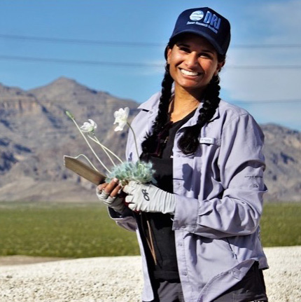EcoLab Tiffany Pereira 430px Tiffany Pereira holding flowers and smiling in a DRI hat and mountains in the background.
