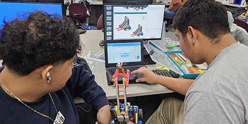 FR students at computer Two students working on a laptop on a table programming a robot.