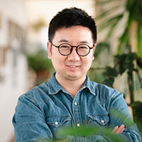Guo Yu wearing glasses photographed in a hallway with plants in the background.