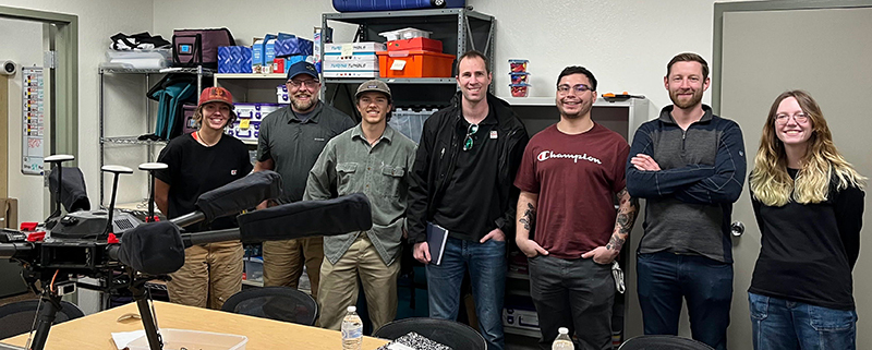 Instructors and students in a group photo with a drone on the table in front of them for Project ROSE.