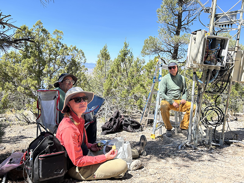 Three researchers sitting around a weather station taking a break from their work.