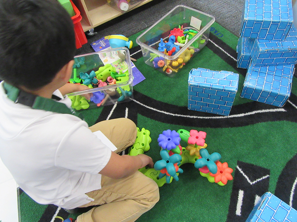 Child playing with building and engineering toys on the green carpet.