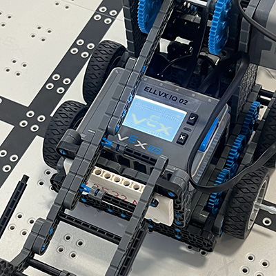 IMG_6221-scaled Up close image of a Vex Robot with wheels on a grid.