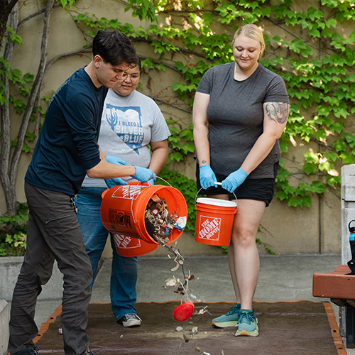 Three interns holding buckets filled with plastic gathered from the beach. One is dumping the debris on to a surface for sorting.