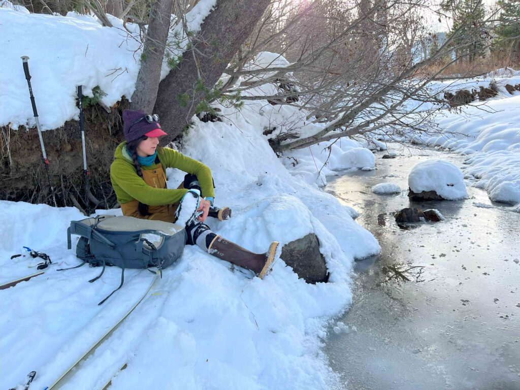 A scientist sitting in the snow next to a frozen stream.