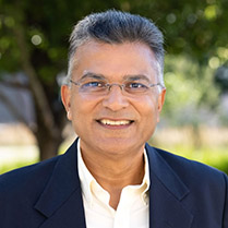 Kumar Naresh 209px Headshot of Naresh Kumar outside with trees in the background and wearing a navy blue suit.