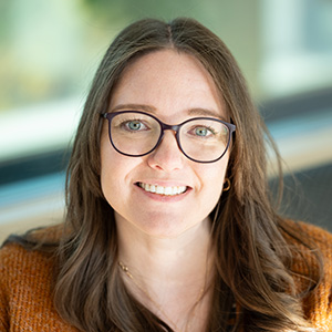 Lauren Cox Headshot 300px Headshot of Lauren smiling and wearing glasses and a orange cardigan.