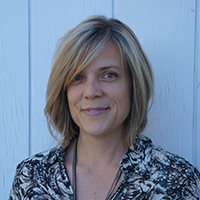 Lynda's headshot outside in natural light in front of a slatted white wall.