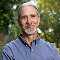 Headshot of Michael Branch in front of trees and wearing a blue collared button down shirt. 