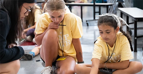 Screenshot Three students on the floor working with robots in a STEM outreach activity.