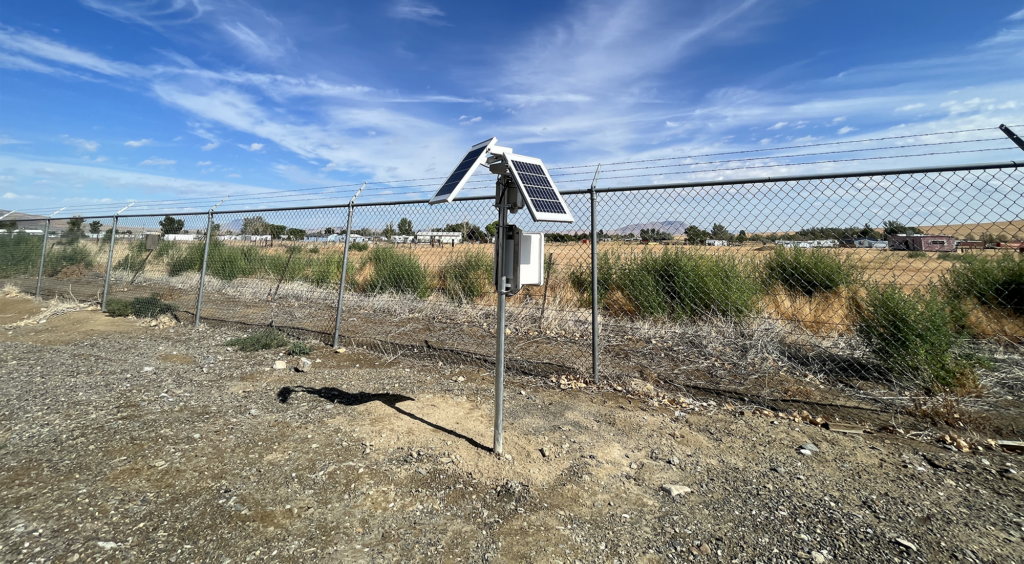 air quality monitoring station in front of a fence with a blue sky in the background.