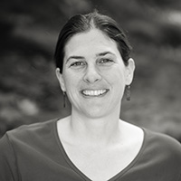Black and White headshot of Rachel Kozloski smiling with her hair pulled back and wearing a v-neck sweater. 