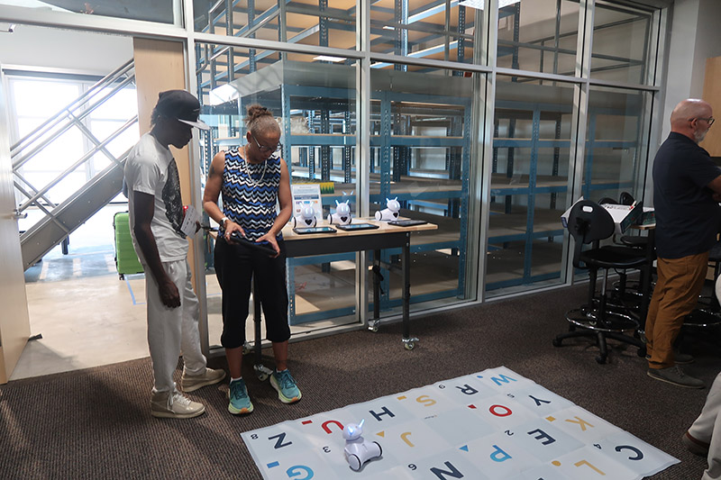 Woman holding a controller looking down at a robot. 