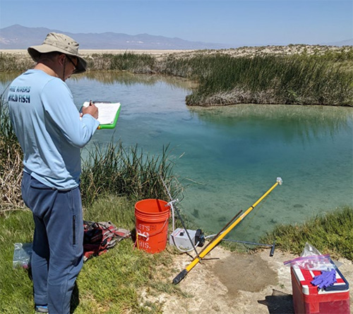 Screenshot Researcher taking notes along a river with testing equipment.