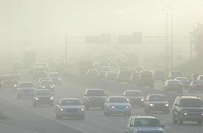 Thick smog hovers over a highway during rush hour traffic.