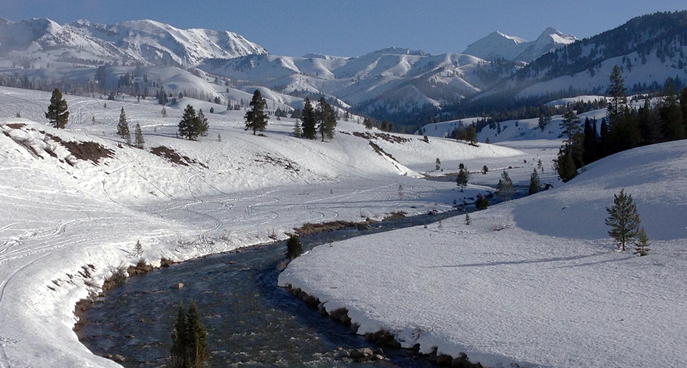 A river winds through a snow covered landscape with mountains in the distance.