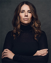 Headshot of Sara Larsen with arms crossed and wearing black against a dark background.