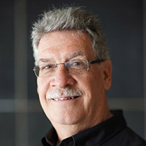 Shew David 209px Headshot of David Shew smiling and wearing glasses against a neutral dark background.