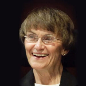 Sue_Wagner_square Sue Wagner wearing glasses and smiling at something just off camera against a black background.