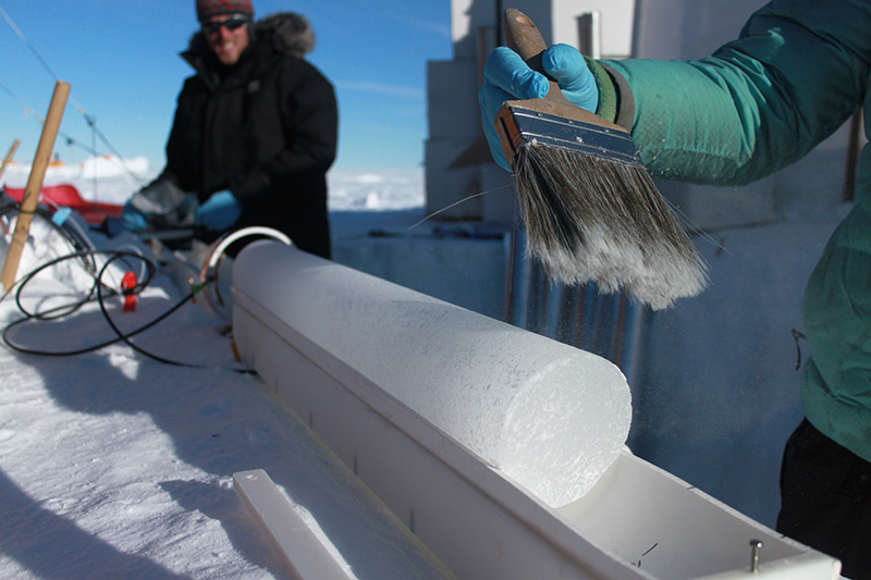 Researcher with a brush working with a ice core on a platform holding is in place.