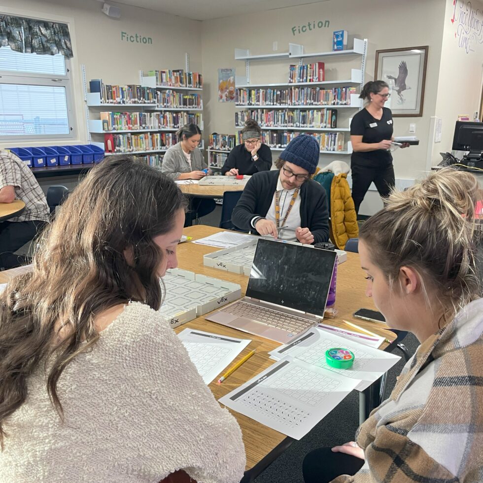 Educators working at tables programming robots to follow a grid during a training.