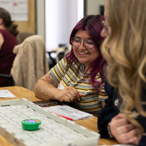Two educators are smiling and working with a small round robot on a grid on a table. 
