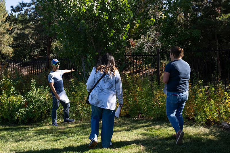An instructor points to a wooded area with trees as students look on.