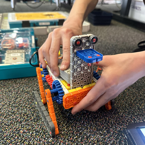 Close up of hands putting together a more complex robot on a table top. 