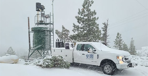 Screenshot DRI Truck in the snow pulled up along side a Cloud Seeding generator.