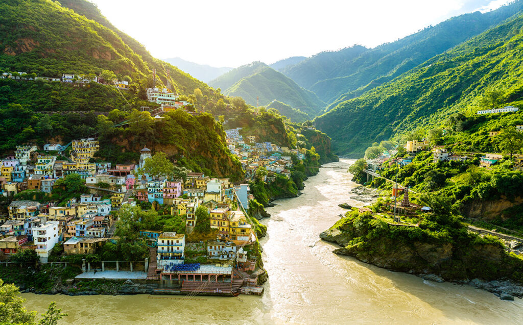 A wide, murky river cutting through a lush green valley with colorful houses on the cliff sides.